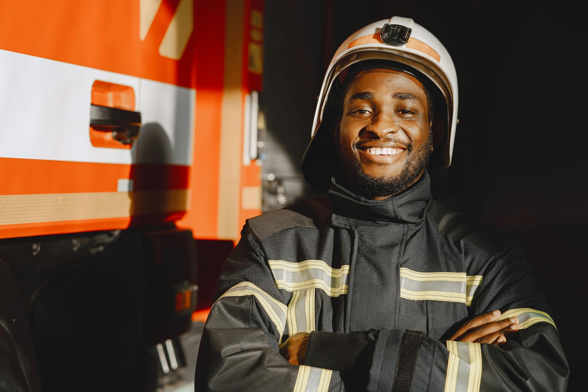 African American firefighter in uniform standing confidently by a fire truck, smiling.