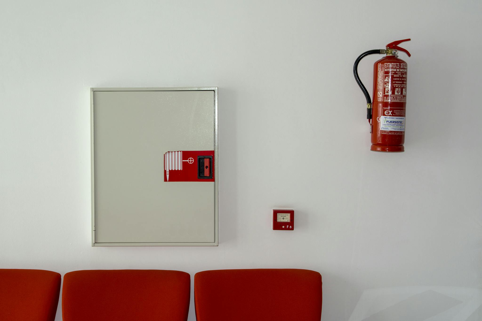 Fire extinguisher and safety equipment mounted on a white wall with red seating below.