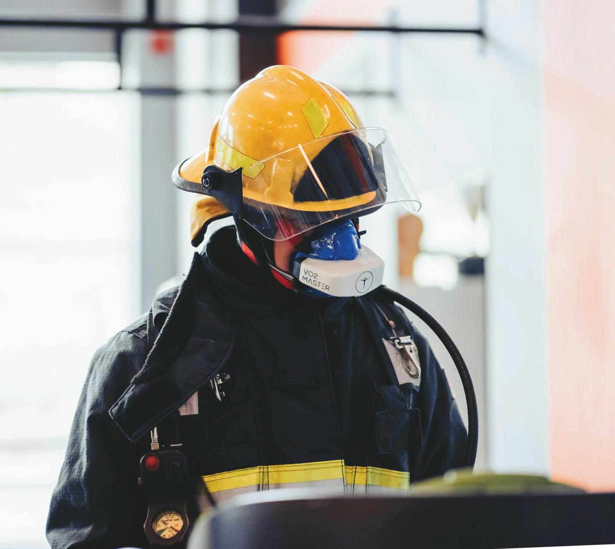 Firefighter wearing full protective gear with helmet and mask indoors.