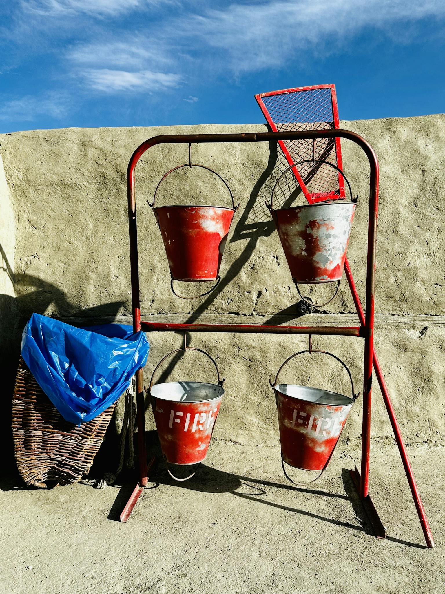Red metal fire buckets on a vintage safety stand against a wall.